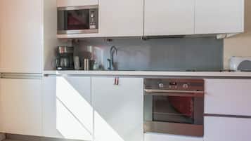 A modern kitchen with white cabinetry, a built-in microwave, a coffee maker, a sink, and an oven.