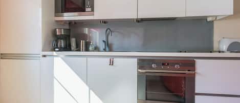 A modern kitchen with white cabinetry, a built-in microwave, a coffee maker, a sink, and an oven.