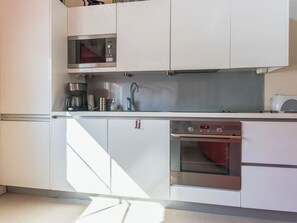 A modern kitchen with white cabinetry, a built-in microwave, a coffee maker, a sink, and an oven. - Poropahta b by Interhome (Kuusamo)
