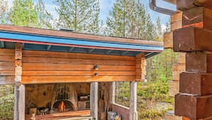 Een houten vakantiehuisje met een stenen open haard, een houten terras en uitzicht op het omliggende bos.