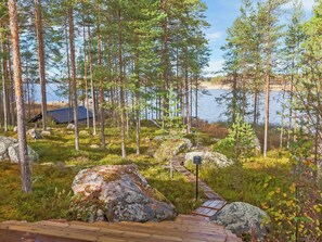 A wooden deck leading to a cabin by a lake, surrounded by tall pine trees and rocky terrain. - Riutankolo by Interhome (Nurmes)