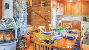 Een gezellig chaletinterieur met een stenen open haard, een houten eettafel gedekt voor vier personen, en een keuken met houten kasten en apparatuur.