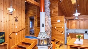 Een gezellig chaletinterieur met een houtkachel, houten wanden, een eethoek en een keuken met houten kastjes.
