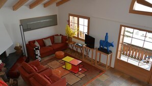 A spacious living room with a red sofa, a coffee table, and a TV on a wooden stand. There is a window with a view of the outside. - Apartment Scapa by Interhome (Schönried)