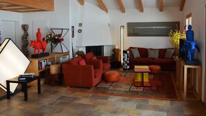 A spacious living room with a high ceiling and exposed wooden beams, furnished with a red sofa, a coffee table, and a fireplace. - Apartment Scapa by Interhome (Schönried)