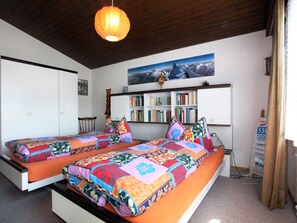 A bedroom with two beds, a bookshelf, and a painting of a mountain landscape.