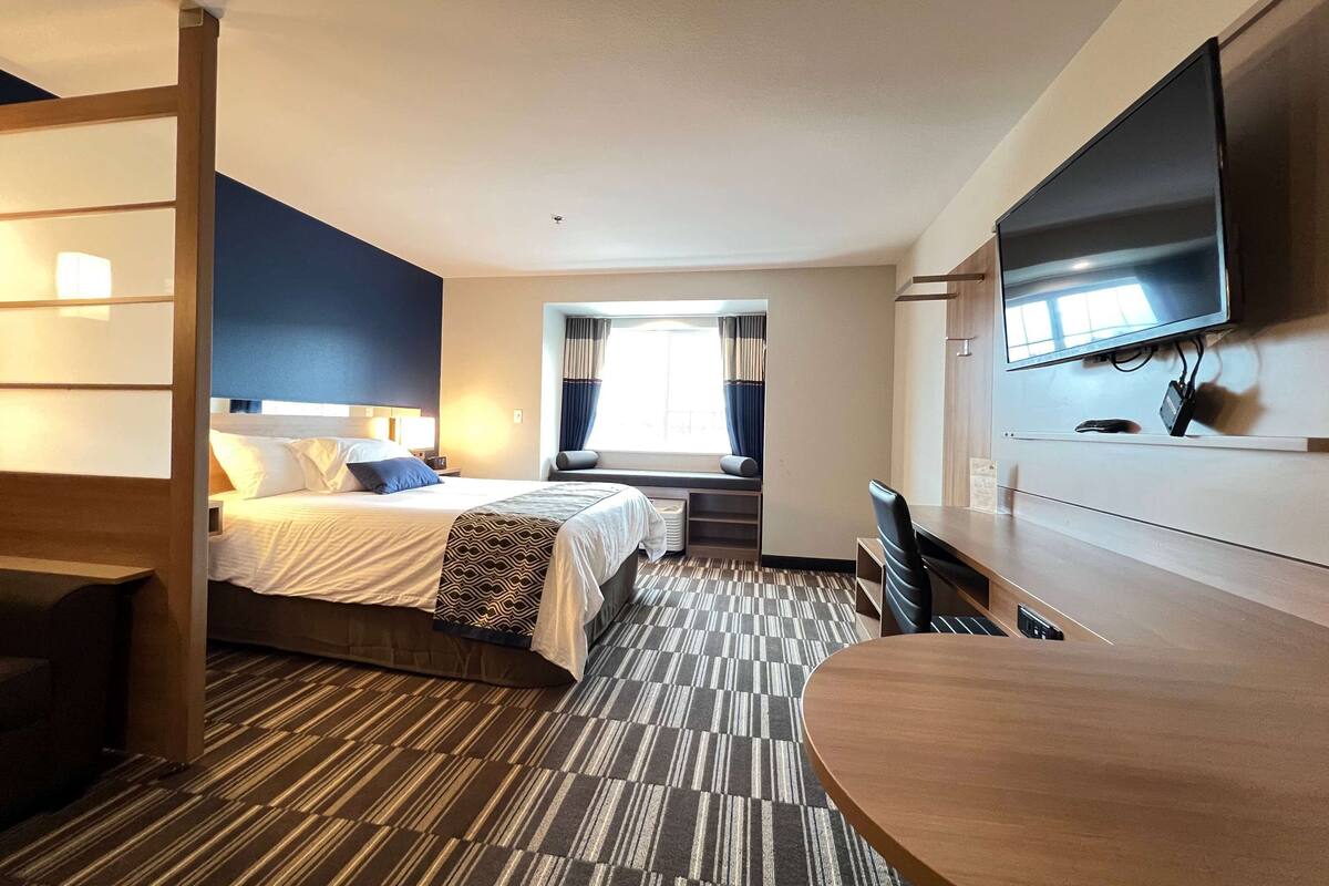 Een hotelkamer met een bed, een bureau, een televisie en een raam met gordijnen.