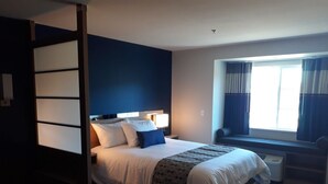 Une chambre d’hôtel moderne avec un grand lit, une table de chevet, une fenêtre avec des rideaux et un banc intégré sous la fenêtre.
