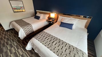Twee enkele bedden met hoofdborden, een nachtkastje met lamp, en een lijst aan de muur.