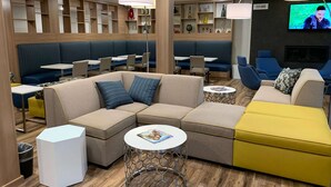 Un espace de détente moderne, aménagé avec des sièges, notamment des canapés et des fauteuils, et un écran de télévision fixé au mur.