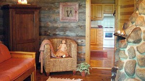 Ein gemütliches Holzhaus-Interieur mit einer Holzbank, einem Korbsessel mit Decke, einem kleinen Tisch mit Kerzen und einer Steinwand.