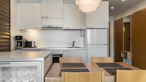 A modern kitchen with white cabinets, a built-in oven, a coffee maker, and a dining area with a wooden table and chairs. - Nordic chalet 9408 by Interhome (Ylläsjärvi)
