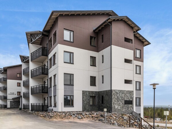 Un edificio residencial de varios pisos con balcones, fachada de piedra y cielo despejado.