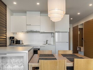 Una cocina moderna con armarios blancos, un refrigerador de acero inoxidable, una cafetera y un comedor con mesa y sillas.