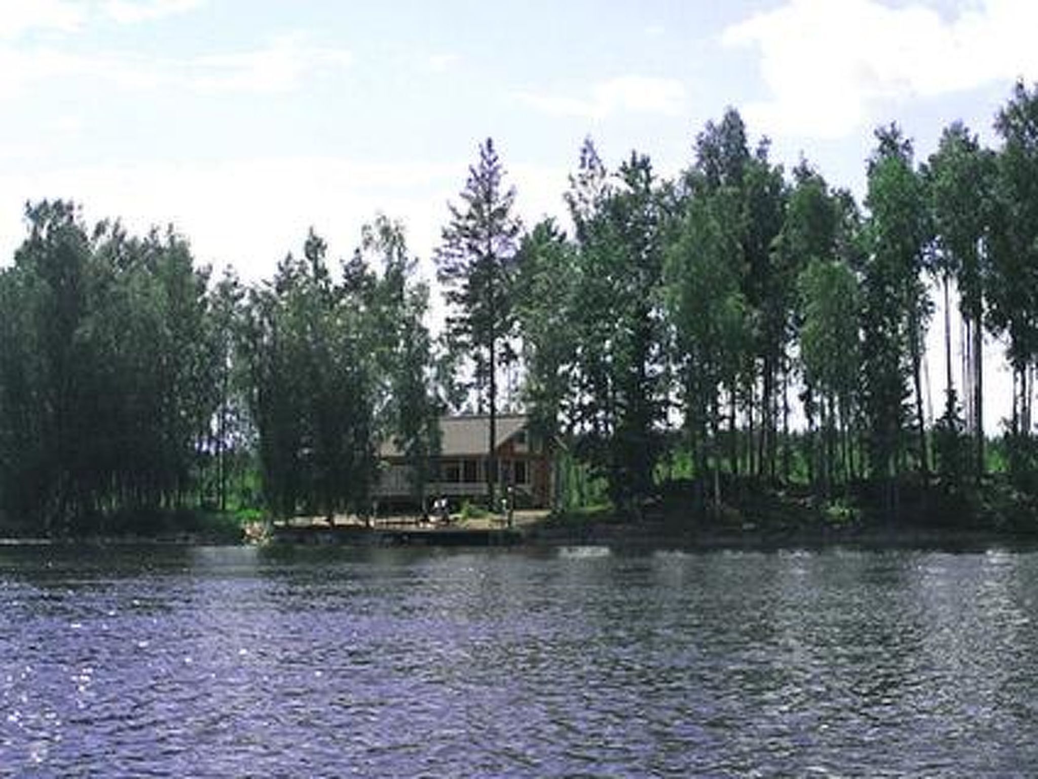 Una cabaña junto a un lago rodeada de árboles altos.