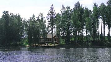 Una cabaña junto a un lago rodeada de árboles altos.
