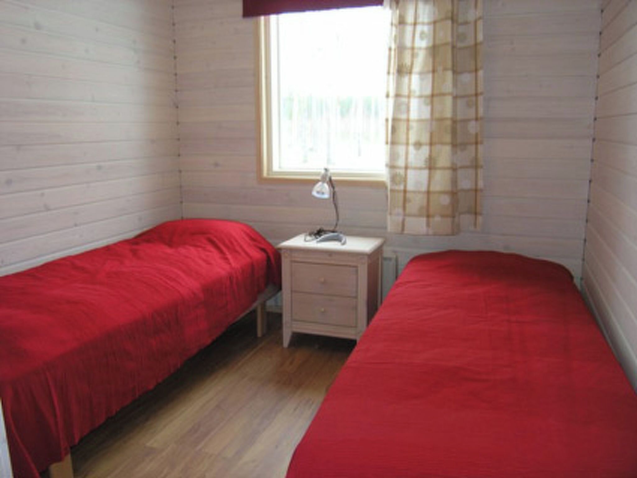 A room with two single beds, a small bedside table with a lamp, and a window with curtains.