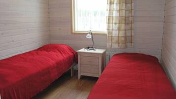 A room with two single beds, a small bedside table with a lamp, and a window with curtains.