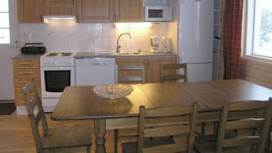 A compact kitchen with wooden cabinets, a microwave, a stove, a dishwasher, and a dining table with chairs. - Pernoo 2 by Interhome (Kotka)