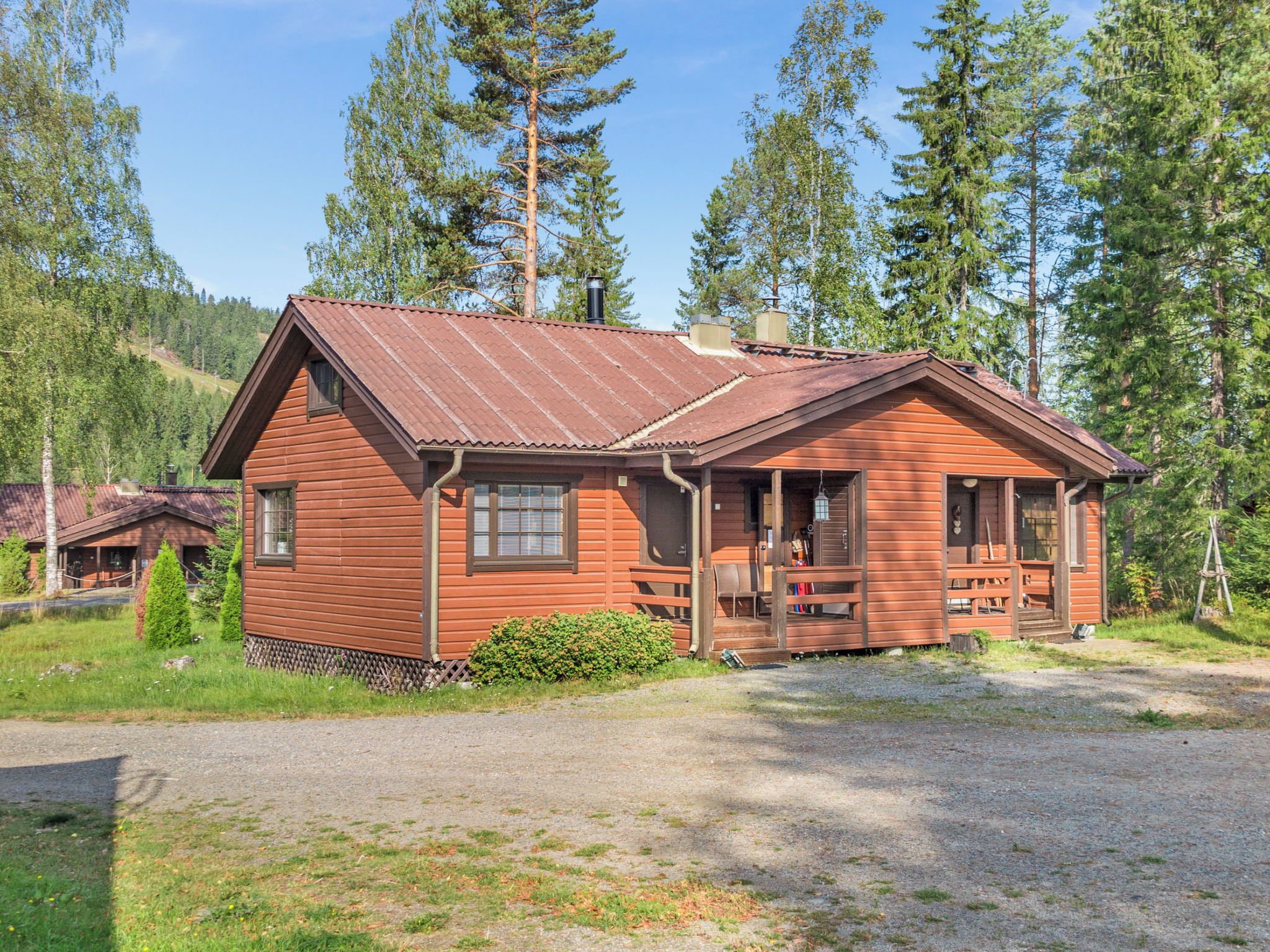 Een houten chalet met een veranda, omringd door bomen en een grindpad.