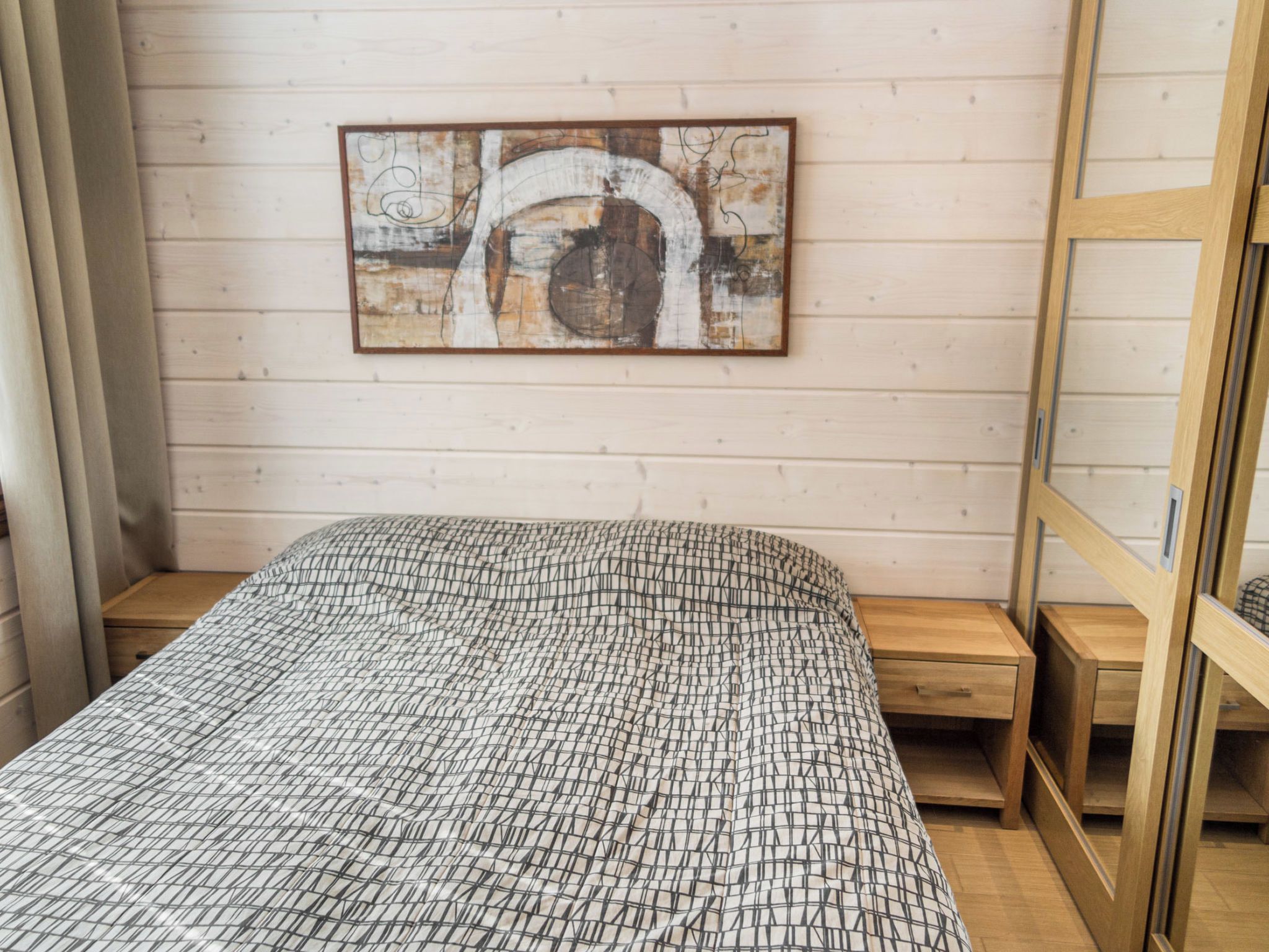 A bedroom with a bed, a wooden headboard, a nightstand, and a wall-mounted artwork.