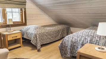 Une petite pièce avec un toit en pente, comprenant deux lits, une table de chevet, une lampe et une fenêtre avec des stores.