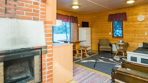 A cozy cabin interior with a brick fireplace, wooden walls, a dining area, and a seating space with a clock on the wall. - Vacation home Rajala by Interhome (Kaavi)