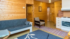 A cozy cabin interior with a wooden interior, a sofa, a chair, a small table, and a kitchenette. - Vacation home Rajala by Interhome (Kaavi)