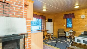 Ein gemütliches Blockhaus mit Kamin, Holzwänden, einer Essecke und einem Fernseher.