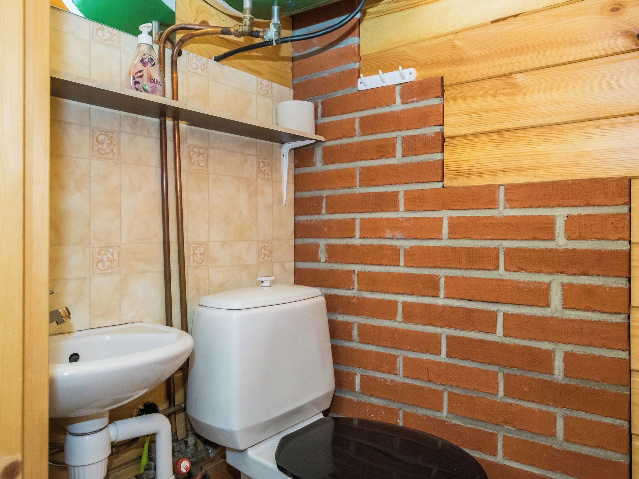 A bathroom with a toilet, sink, and a wooden wall with a brick pattern.