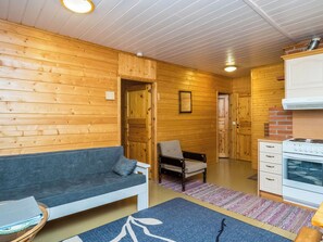 A cozy cabin interior with a sofa, a chair, a small kitchen area with a stove, and wooden walls. - Vacation home Rajala by Interhome (Kaavi)