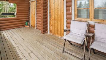 A log cabin with a wooden deck, two doors, and two white chairs.
