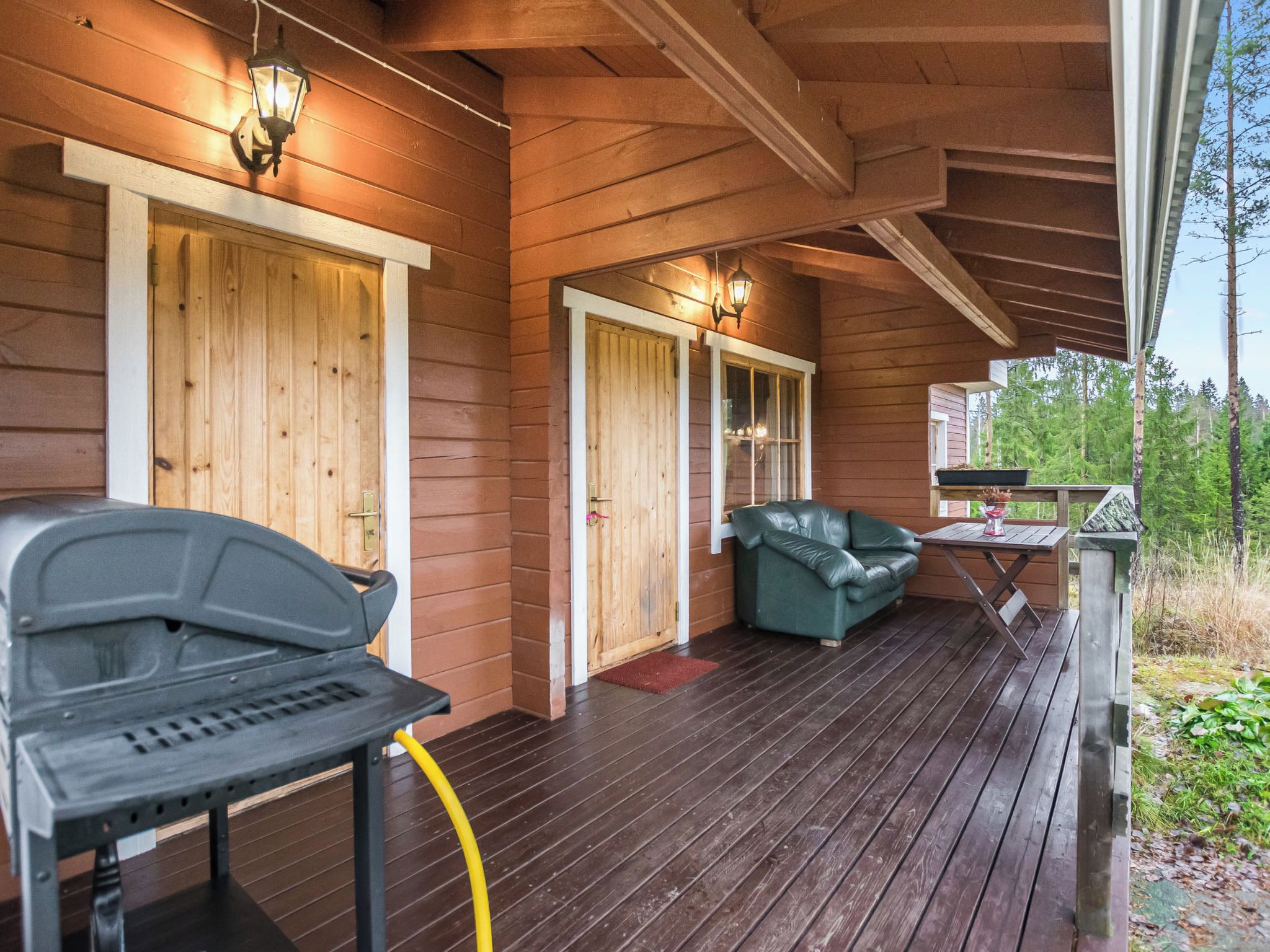 Een houten terras met een barbecue, een bank en een tafel.