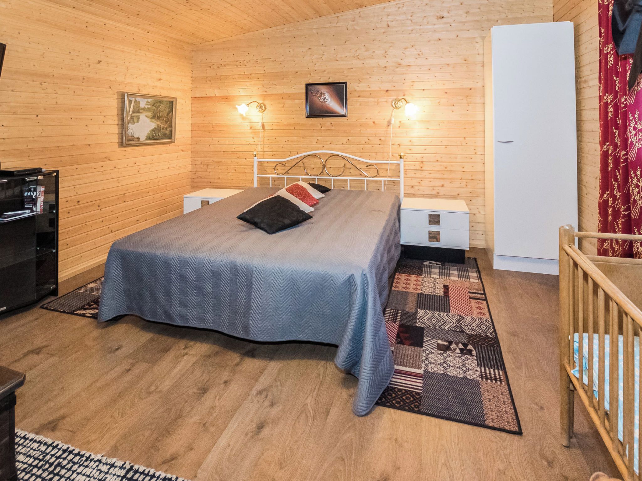 A room with a bed, bedside tables, a television, and a refrigerator.