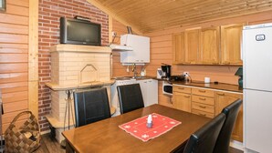 A compact kitchen with a brick wall, wooden cabinets, a stove, and a refrigerator. - Mäntymäki by Interhome (Raasepori)