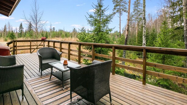 A wooden deck with wicker furniture and a table, overlooking a forested area. - Mäntymäki by Interhome (Raasepori)
