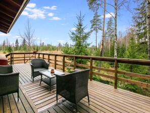 A wooden deck with wicker furniture and a table, overlooking a forested area. - Mäntymäki by Interhome (Raasepori)