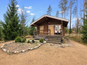 A log cabin with a porch, surrounded by a forest.