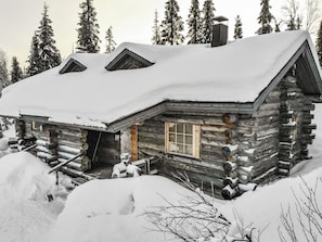 Una cabaña de troncos con techo nevado, chimenea y ventana con contraventanas.