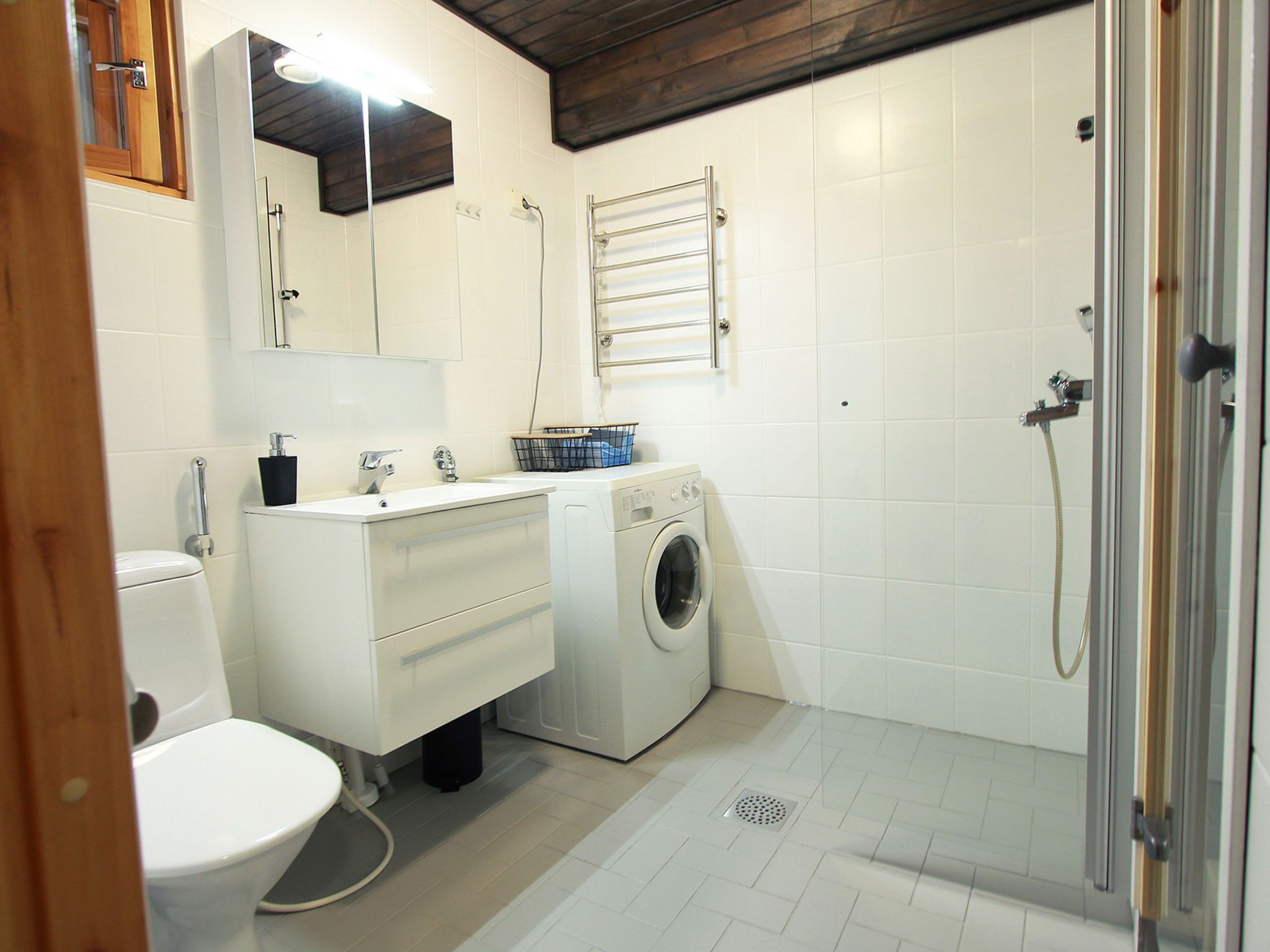 A compact bathroom with a toilet, sink, washing machine, and shower.