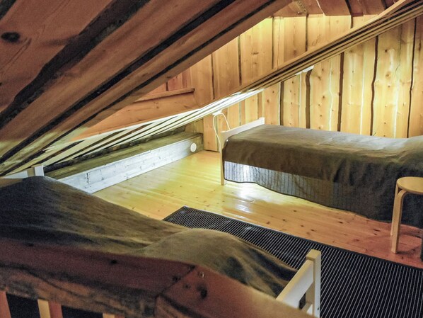 Ein kleines Schlafzimmer im Dachgeschoss, aus Holz, mit zwei Betten und einem Sessel.