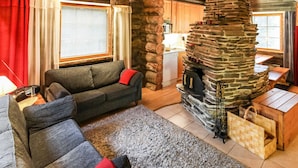 Ein gemütliches Blockhaus-Interieur mit Kamin aus Stein, einer Couch und einem Essbereich.