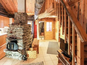 A log cabin interior with a stone fireplace, wooden walls, and a television.