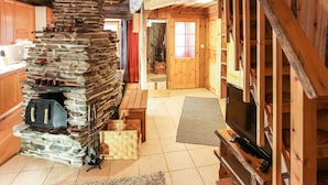Ein rustikales Blockhaus-Interieur mit Kamin aus Stein, Holzbalken und einem Fernseher.