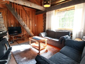 L’intérieur d’un chalet accueillant, avec un escalier en bois, un téléviseur, un canapé et une table basse.