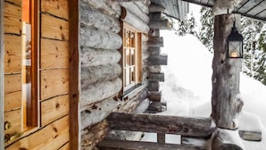 Eine Blockhütte mit Holztür und -fenstern, einem Steinkamin und einer Laterne auf der Veranda.