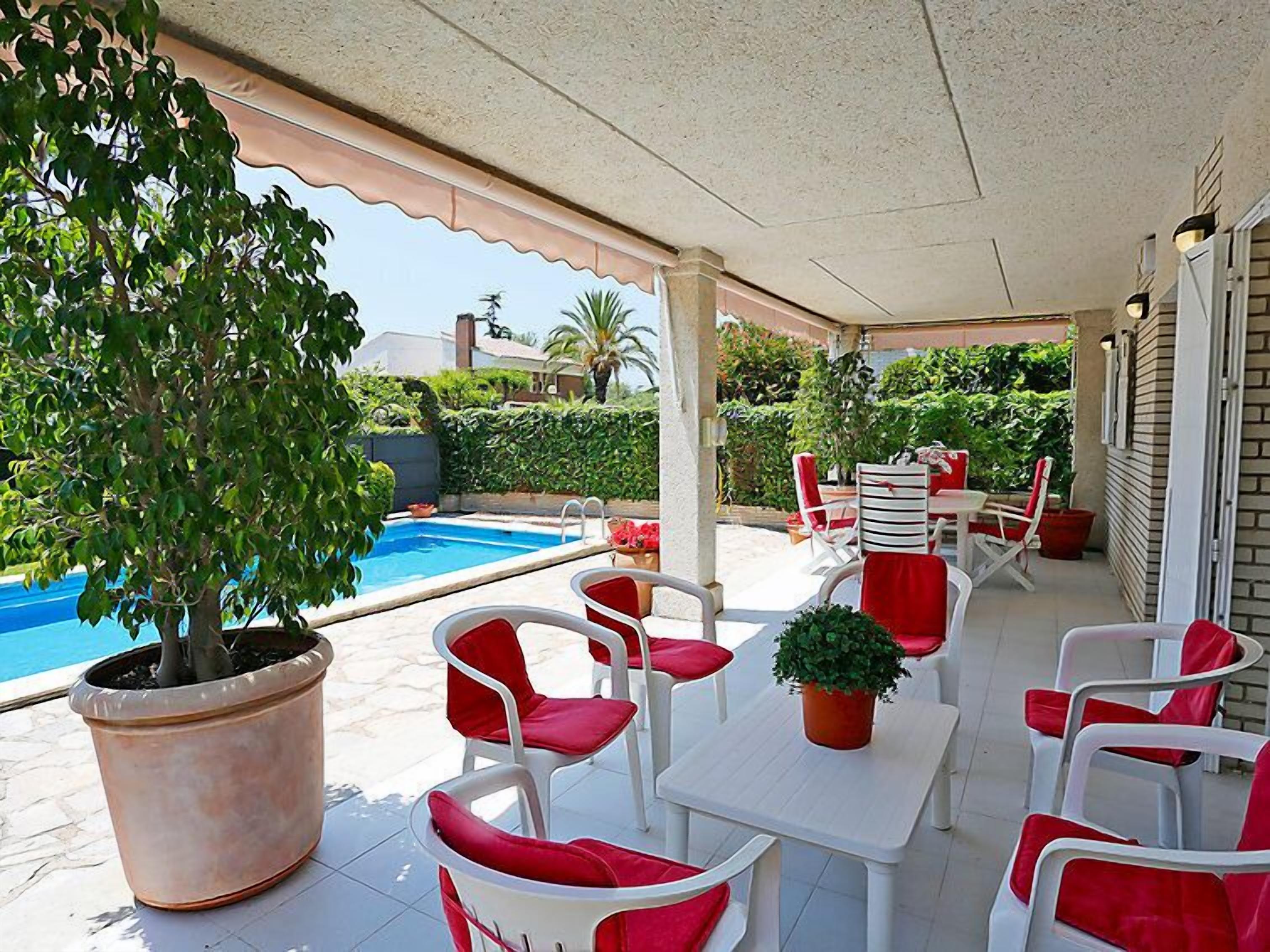Un espace extérieur abrité avec des chaises blanches et rouges, une table et une plante en pot.
