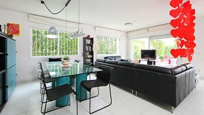 A modern living space with a glass dining table, black leather sofa, and a TV.