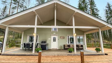 A two-story building with a covered porch, a grill, and outdoor seating.