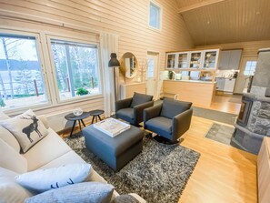 Een moderne woonkamer met een open haard, een keuken op de achtergrond en een groot raam met uitzicht op bomen.